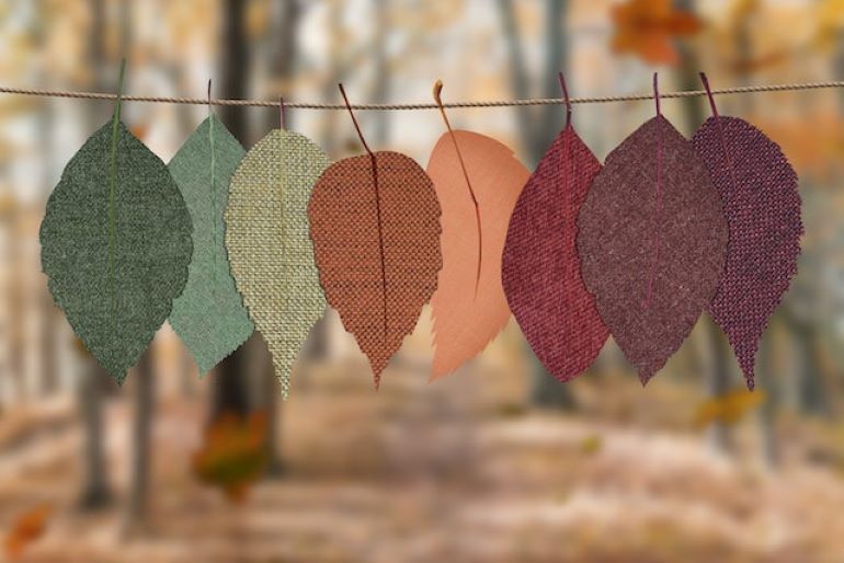 Colorful autumn leaves in green, orange, and burgundy hues hanging on a rope, showcasing fall’s vibrant palette for home decor.