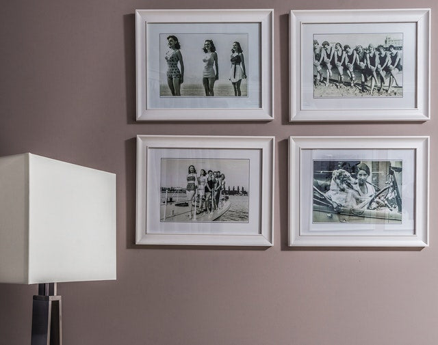 Vintage black and white photos displayed in white frames on a mauve wall.