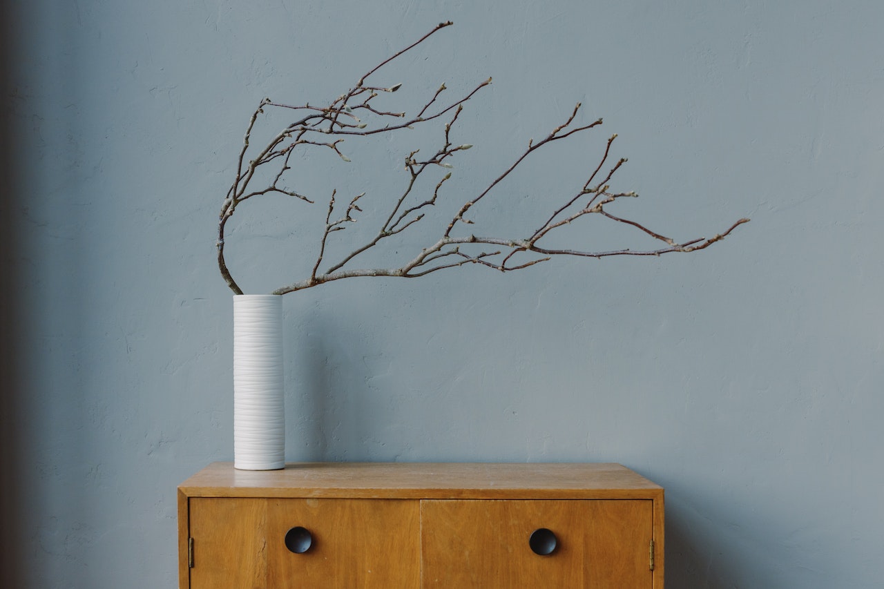 white textured vase with bare branches on wooden cabinet against muted blue wall