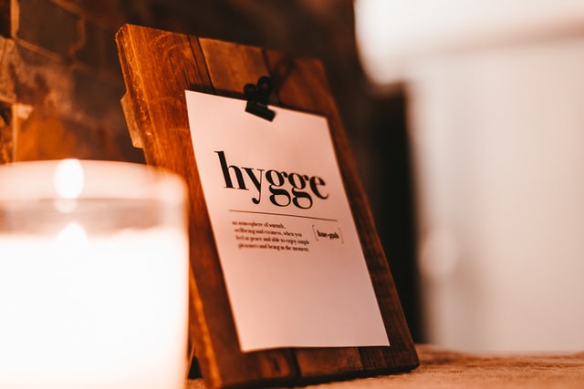 A wooden sign displaying the word ‘hygge’ with a lit candle beside it, evoking cozy Scandinavian ambiance.