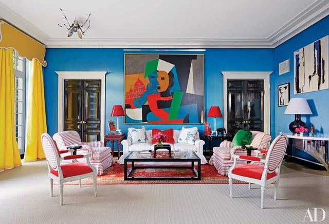 Celebrate Your Home With a Splash of Color-Brush Point Studio(Vibrant living room with bold blue walls, abstract artwork, red and white striped chairs, and colorful décor – Architectural Digest)