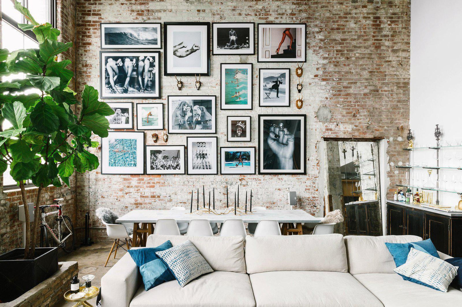 7 Gorgeous Gallery Walls That Will Inspire You to Create Your Own-Brush Point Studio(Industrial living room gallery wall with black and white photographs arranged on exposed brick wall above a dining area.)